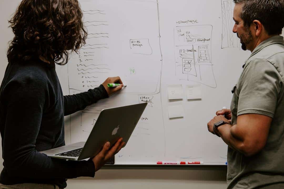 Two people collaborating at a whiteboard with diagrams and notes in an office setting