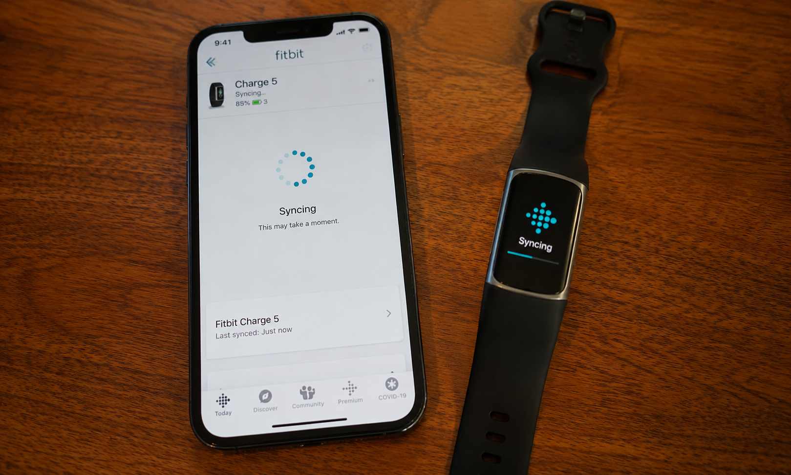 iphone beside a fitbit charge 5 on a wooden table, with both screens showing active syncing progress