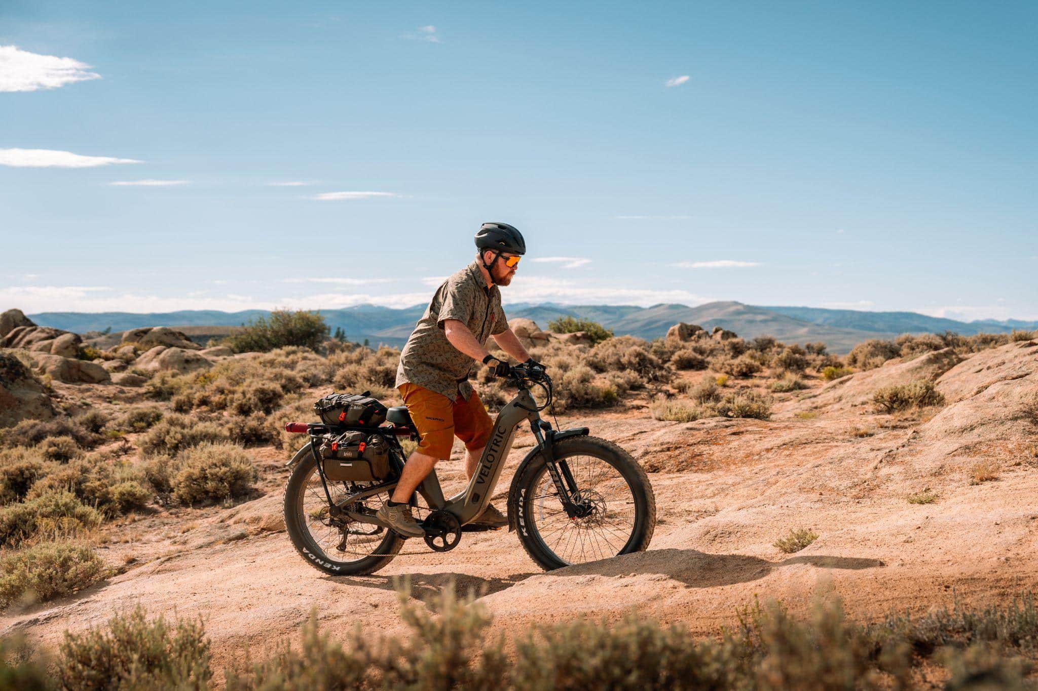 Cyclist riding an electric bike on rocky desert terrain under clear blue sky