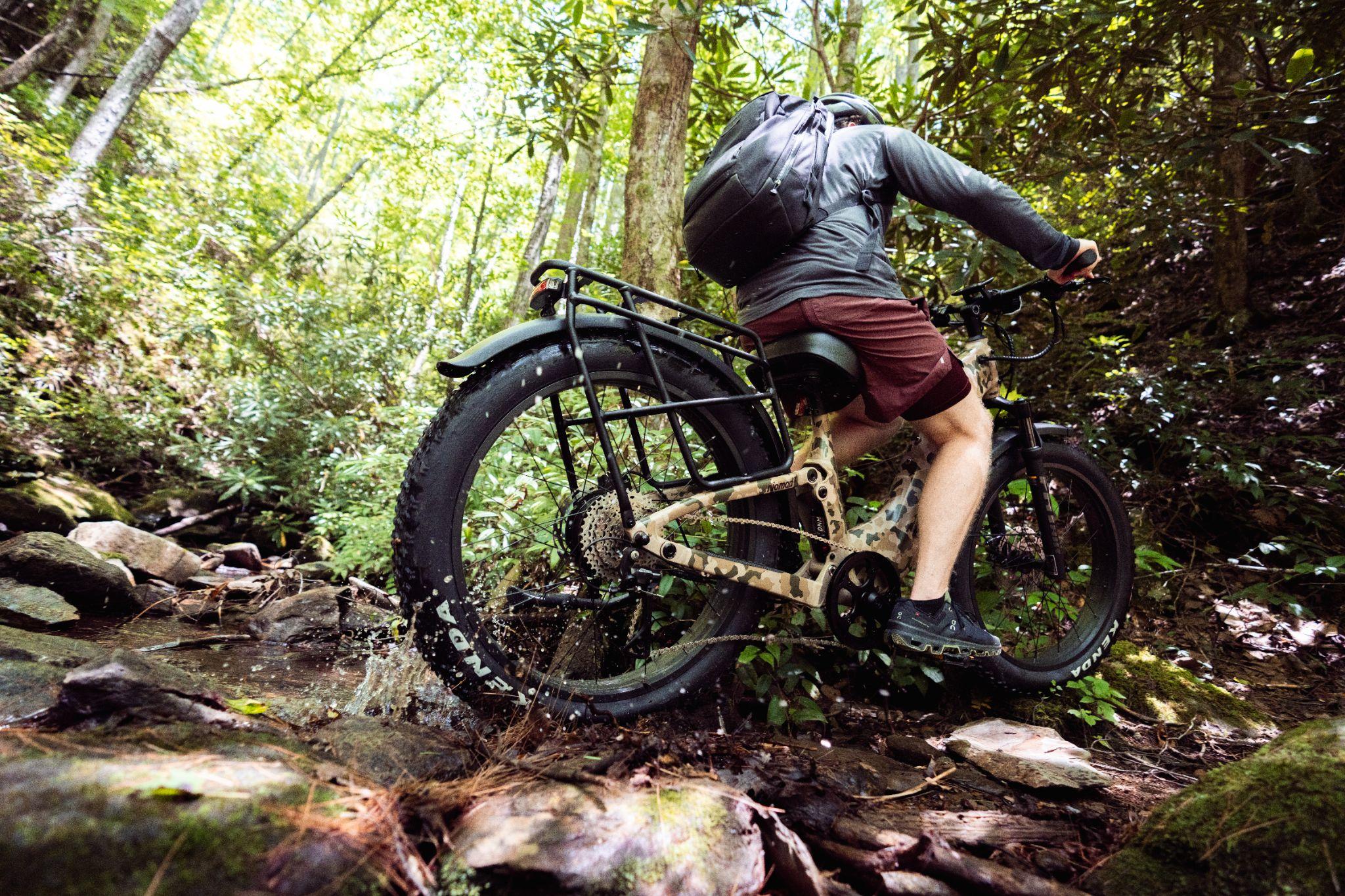 Cyclist in shorts riding mountain bike through forested terrain and rocky streambed