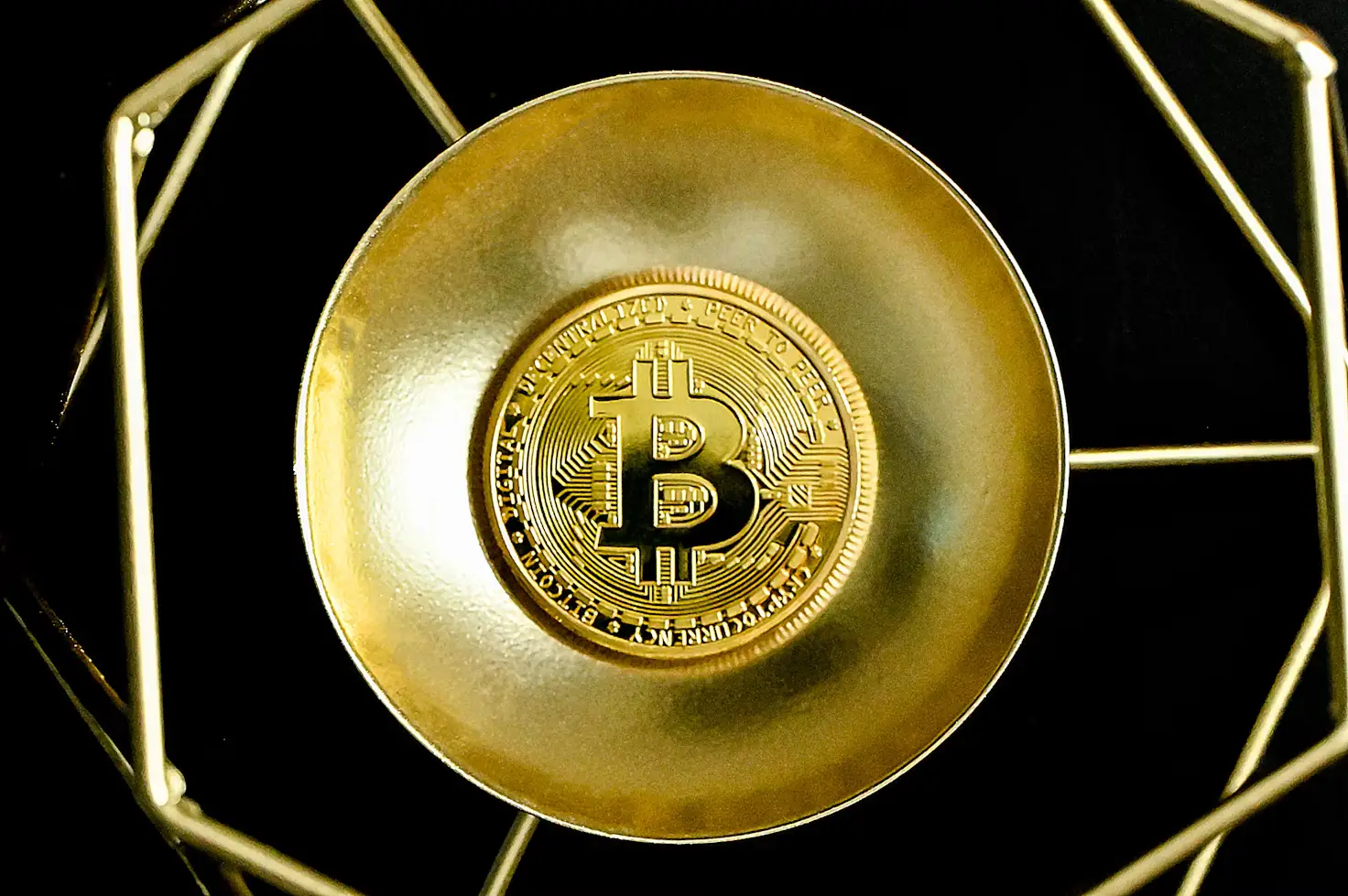 Gold Bitcoin coin on reflective surface with geometric metallic frame in dark setting